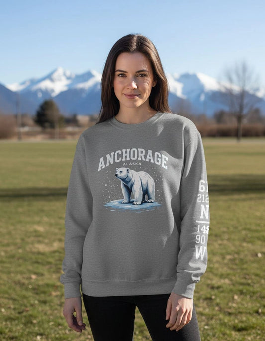 Woman wearing a gray sweatshirt with a polar bear graphic and 'Anchorage' text, standing in a field with mountains in the background.