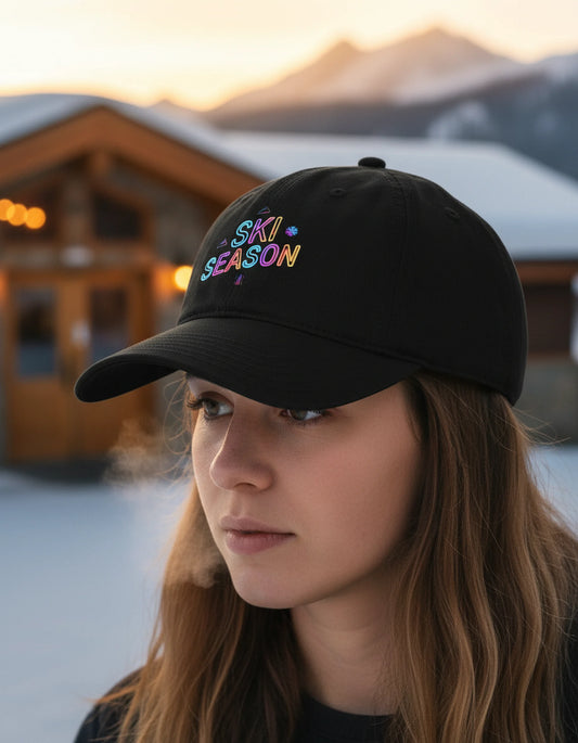 Person wearing a black cap with 'Ski Season' text in colorful letters, standing in a snowy landscape.