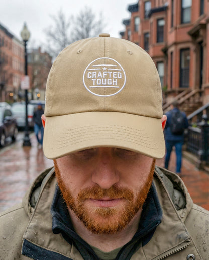 Man wearing a beige cap with 'Crafted Tough' logo on a city street.
