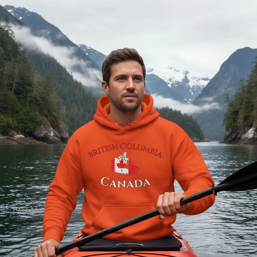 Man in an orange 'British Columbia, Canada' hoodie kayaking with mountains in the background