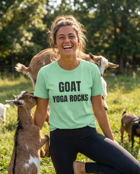 Woman wearing a 'GOAT YOGA ROCKS' shirt surrounded by goats in a field.