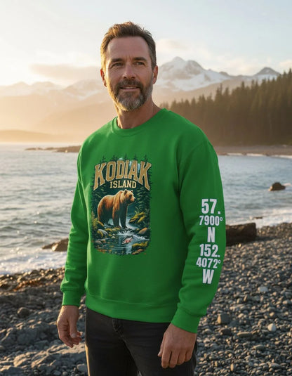 Man wearing a green sweatshirt with a bear graphic and text standing on a beach with mountains in the background.
