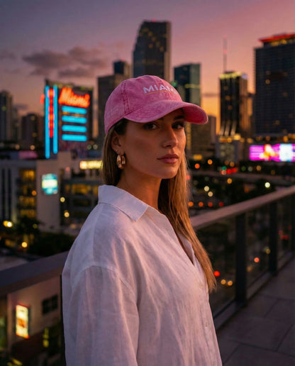 Woman at sunset wearing Miami cap against a city backdrop.