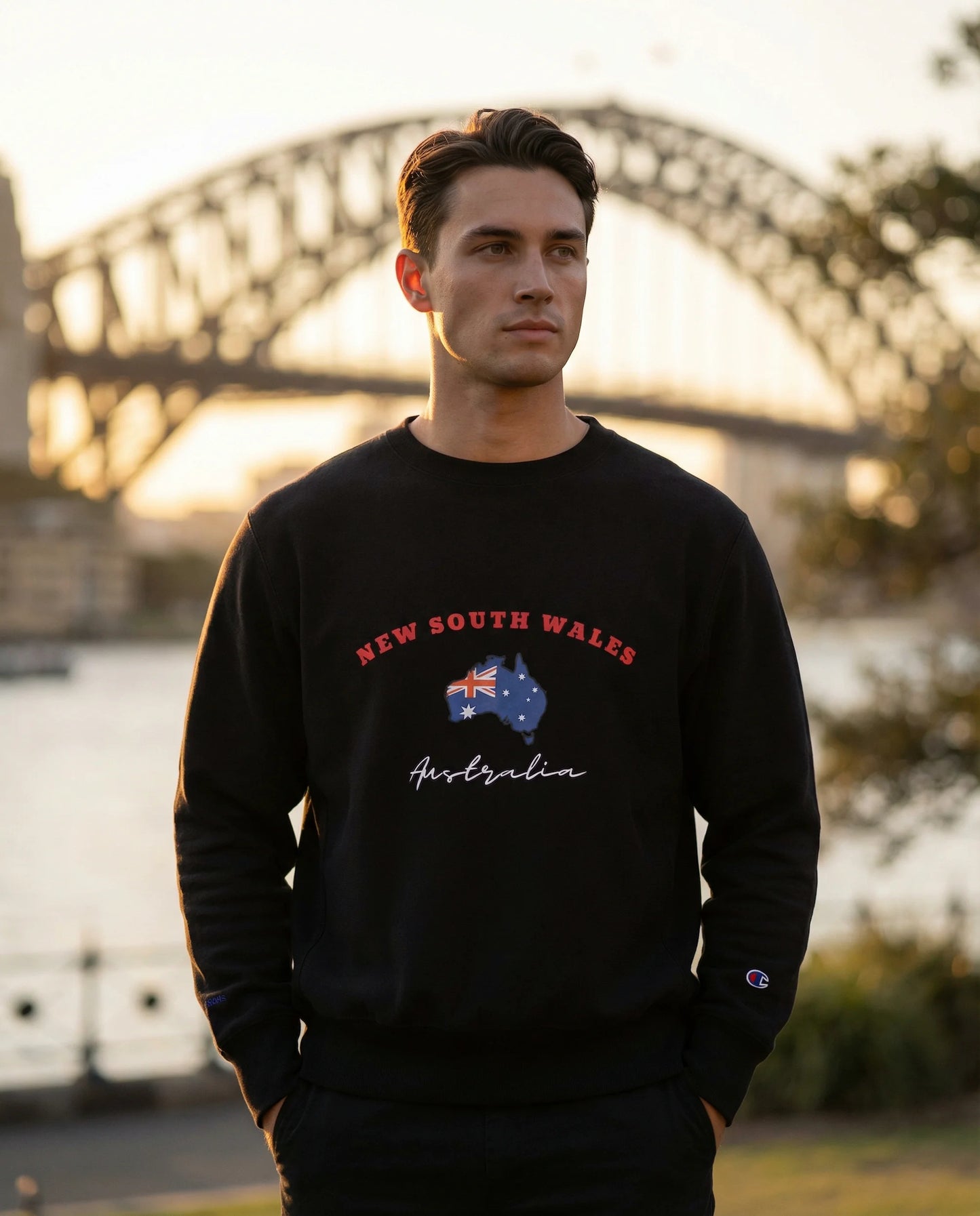 Person wearing a black sweatshirt with 'New South Wales Australia' design in front of a bridge.