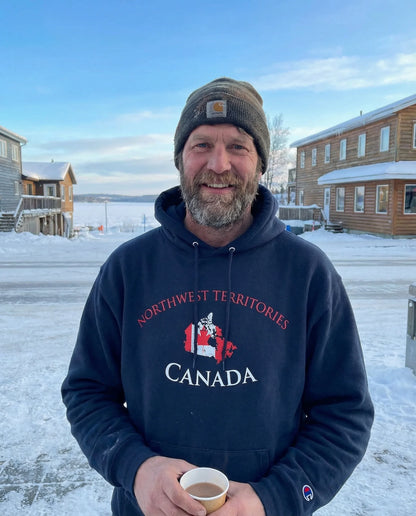 Man wearing a hoodie with 'Northwest Territories Canada' text, holding a cup outdoors in winter.