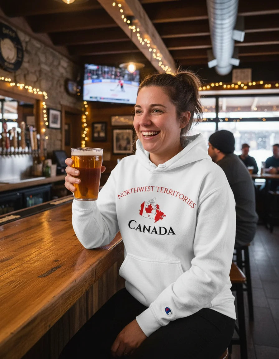 Person wearing a hoodie with 'Northwest Territories Canada' design, holding a beer in a bar setting.