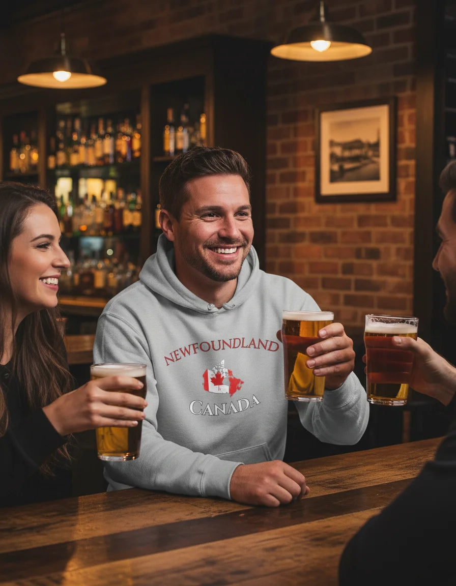 Man in a hoodie with 'Newfoundland Canada' design holding a beer, sitting at a bar with two women.