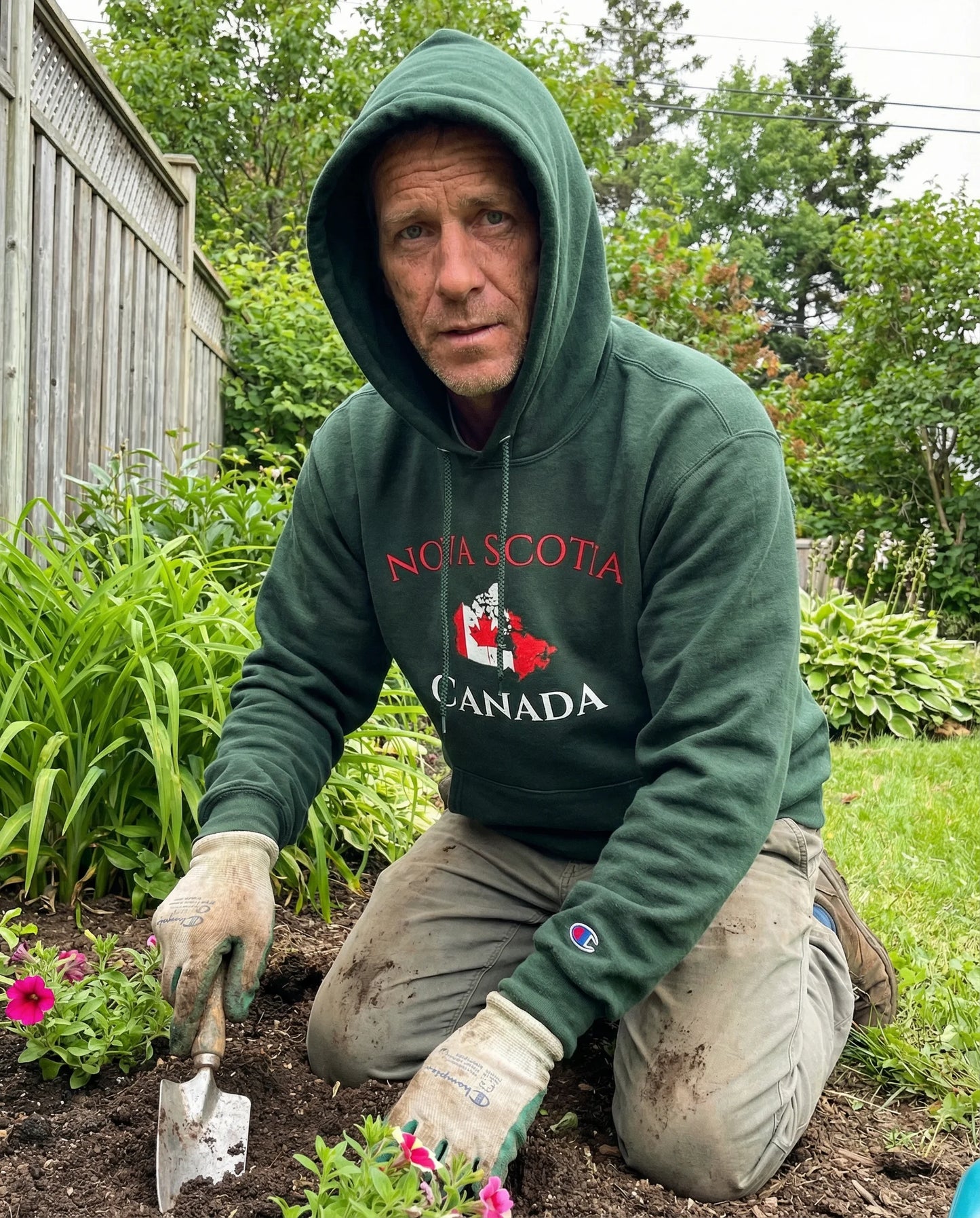 Man in a green 'Nova Scotia Canada' hoodie gardening outdoors.
