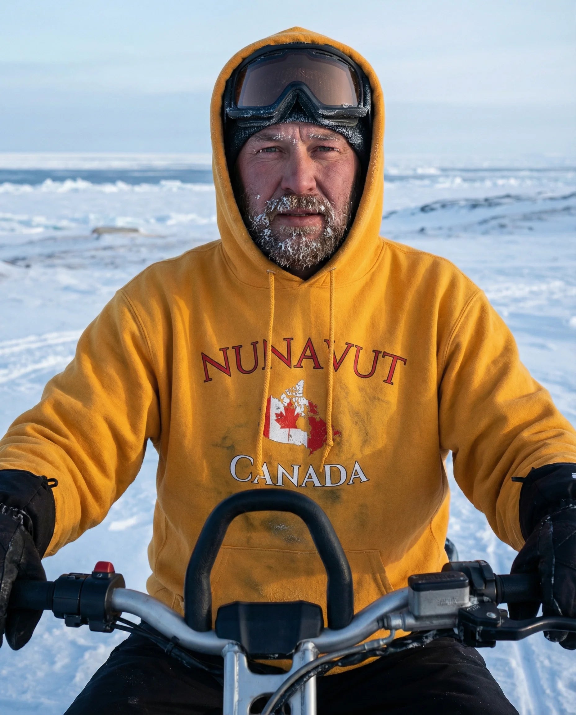 Person wearing a yellow 'Nunavut Canada' hoodie on a snowmobile in a snowy landscape.