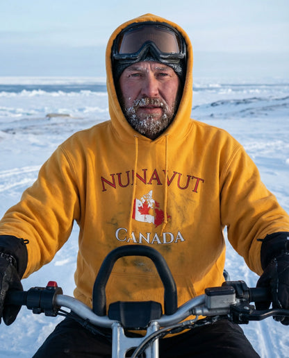Person wearing a yellow 'Nunavut Canada' hoodie on a snowmobile in a snowy landscape.