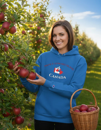 Woman in a blue hoodie with 'Canada' text holding apples in an orchard