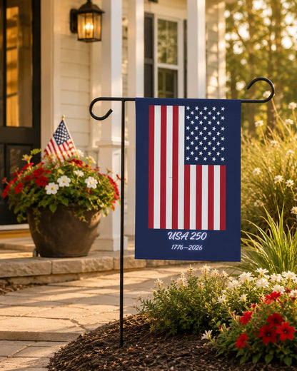 American flag garden flag with 'USA 250' text in a garden setting.