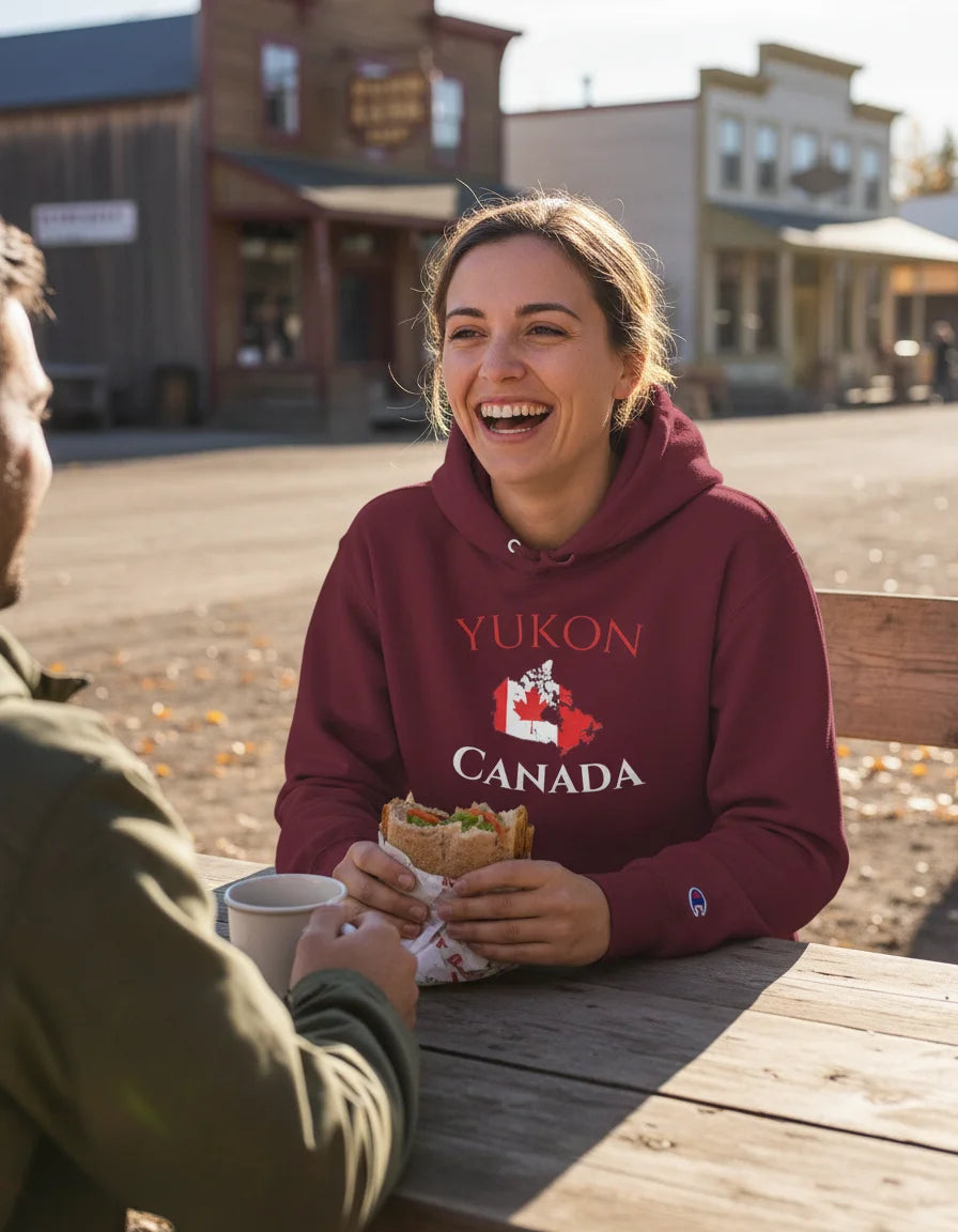 Person wearing a 'Yukon Canada' hoodie sitting at a wooden table with another person, enjoying a meal.